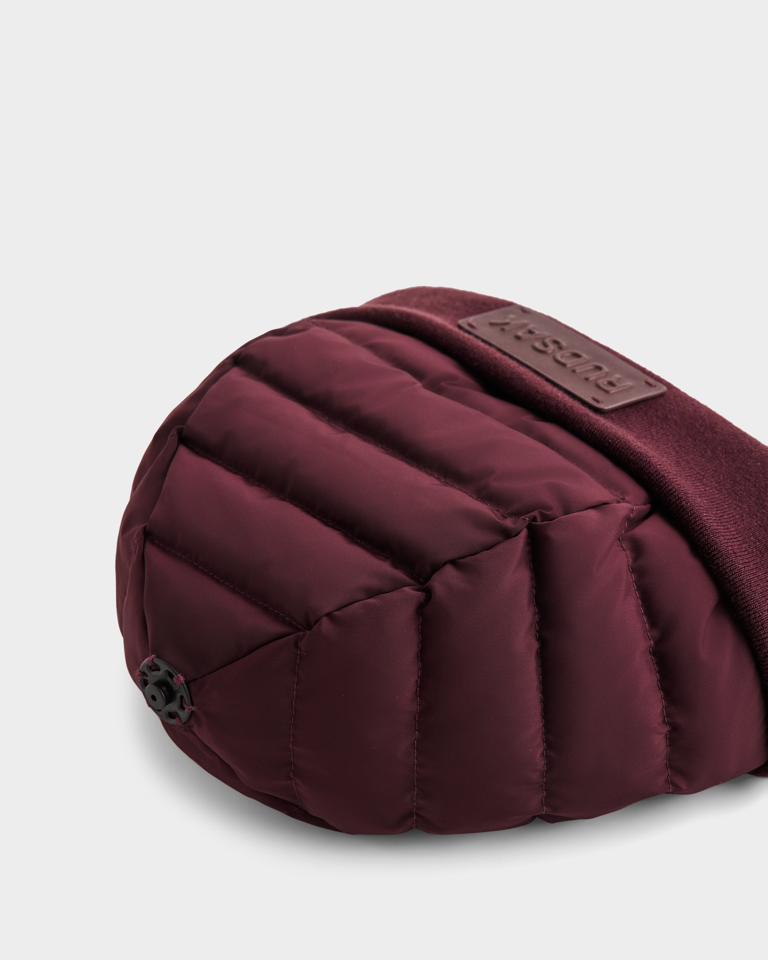 Close-up of the GALA - 8424514 Bordeaux by Rudsak, a maroon quilted bag with premium down insulation, textured strap, black adjustable toggle, and a rectangular embossed brand label.