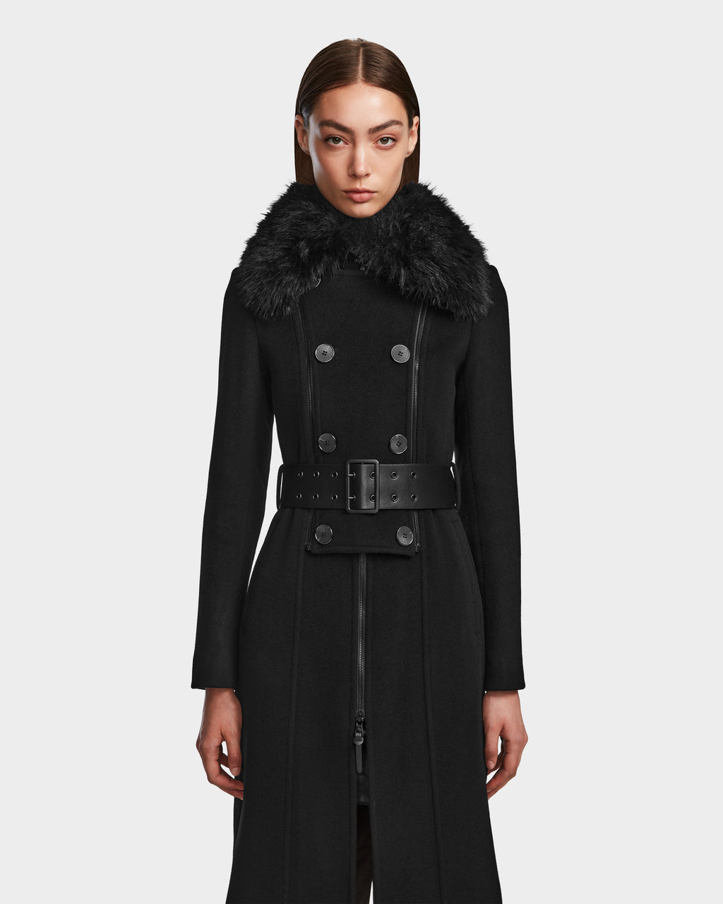 A woman stands facing forward against a plain white background, wearing the Rudsak VIRGINIE - 8124696 Black coat, a long wool and cashmere design with a wide belt and large removable faux fur collar.