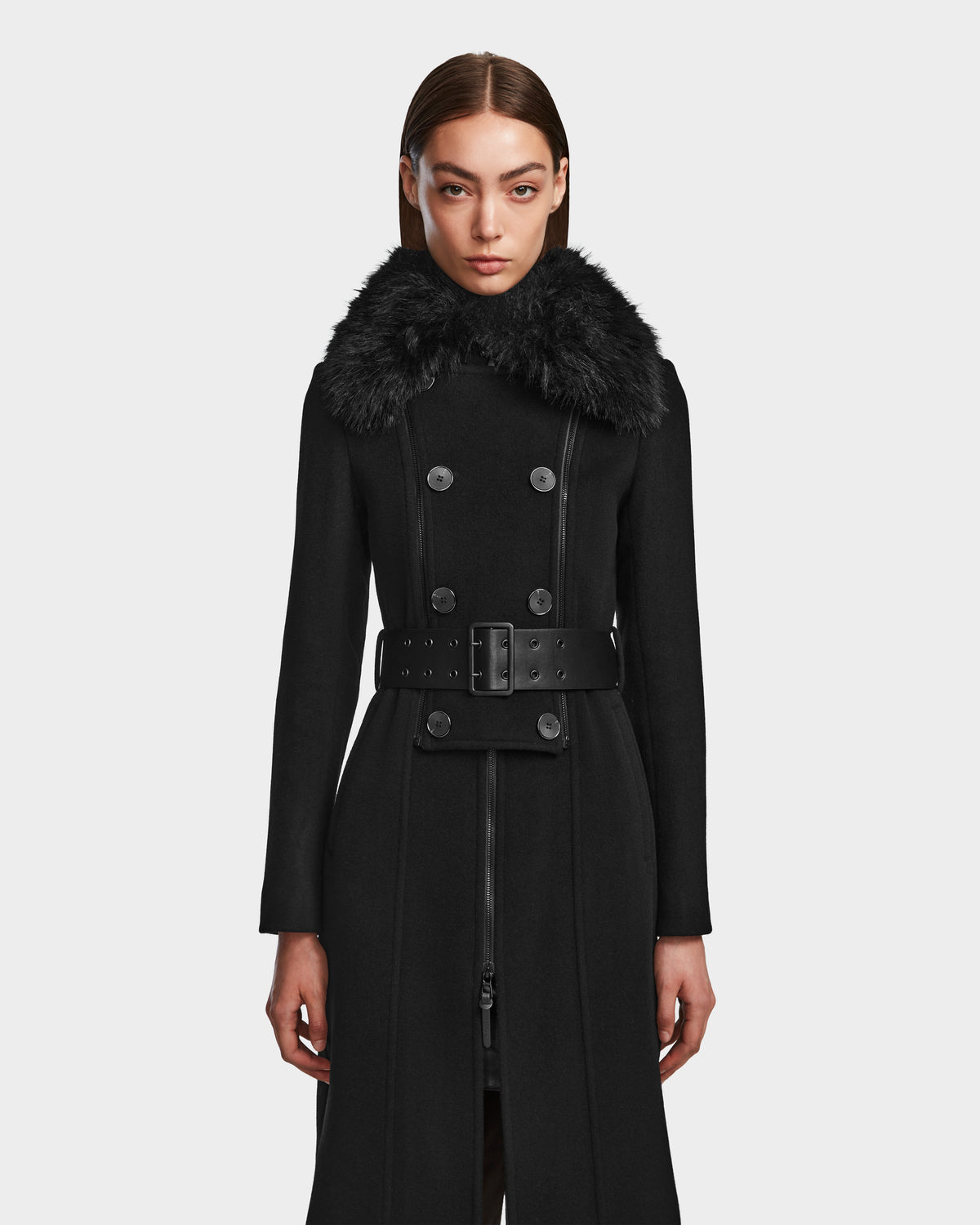 A woman stands facing forward against a plain white background, wearing the Rudsak VIRGINIE - 8124696 Black coat, a long wool and cashmere design with a wide belt and large removable faux fur collar.