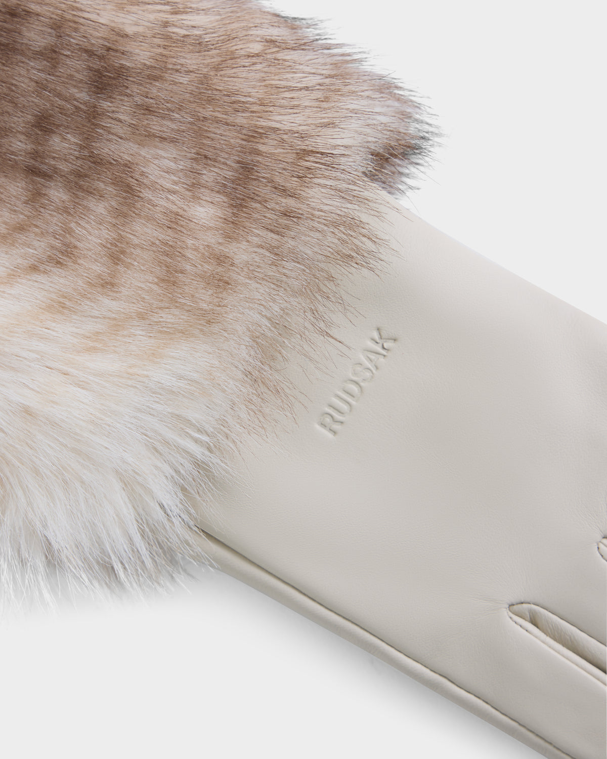 A close-up of the ZAYLA - 8426712 Vanilla glove by Rudsak, crafted from cream-colored leather with soft brown-and-white fur trim. The brand name “RUDSAK” is embossed on the leather near the wrist.