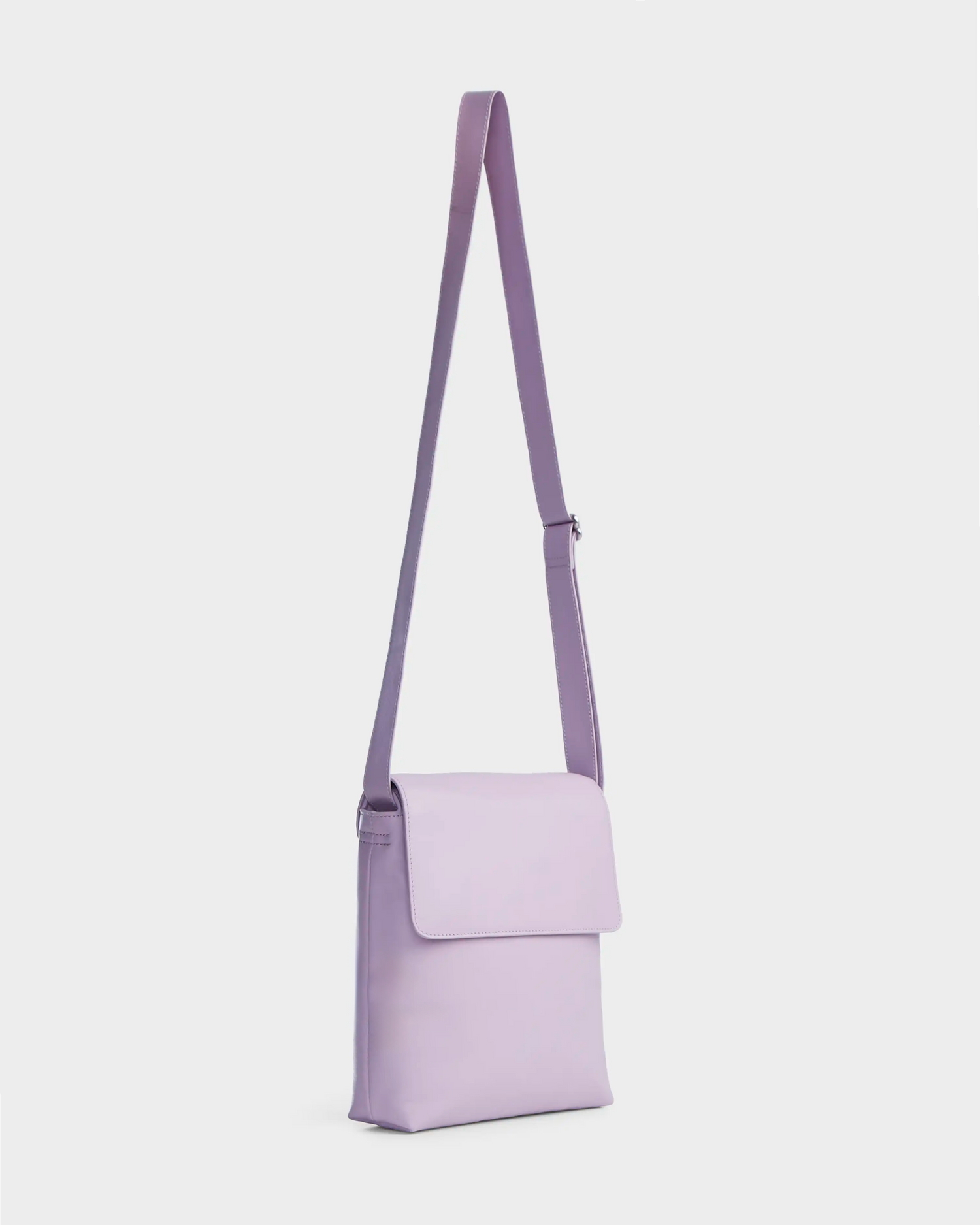 The Rudsak MADDY - 8319536 Lilac Foam is a minimalist, rectangular lavender leather messenger bag with a long adjustable strap and front flap closure, shown on a plain white background.