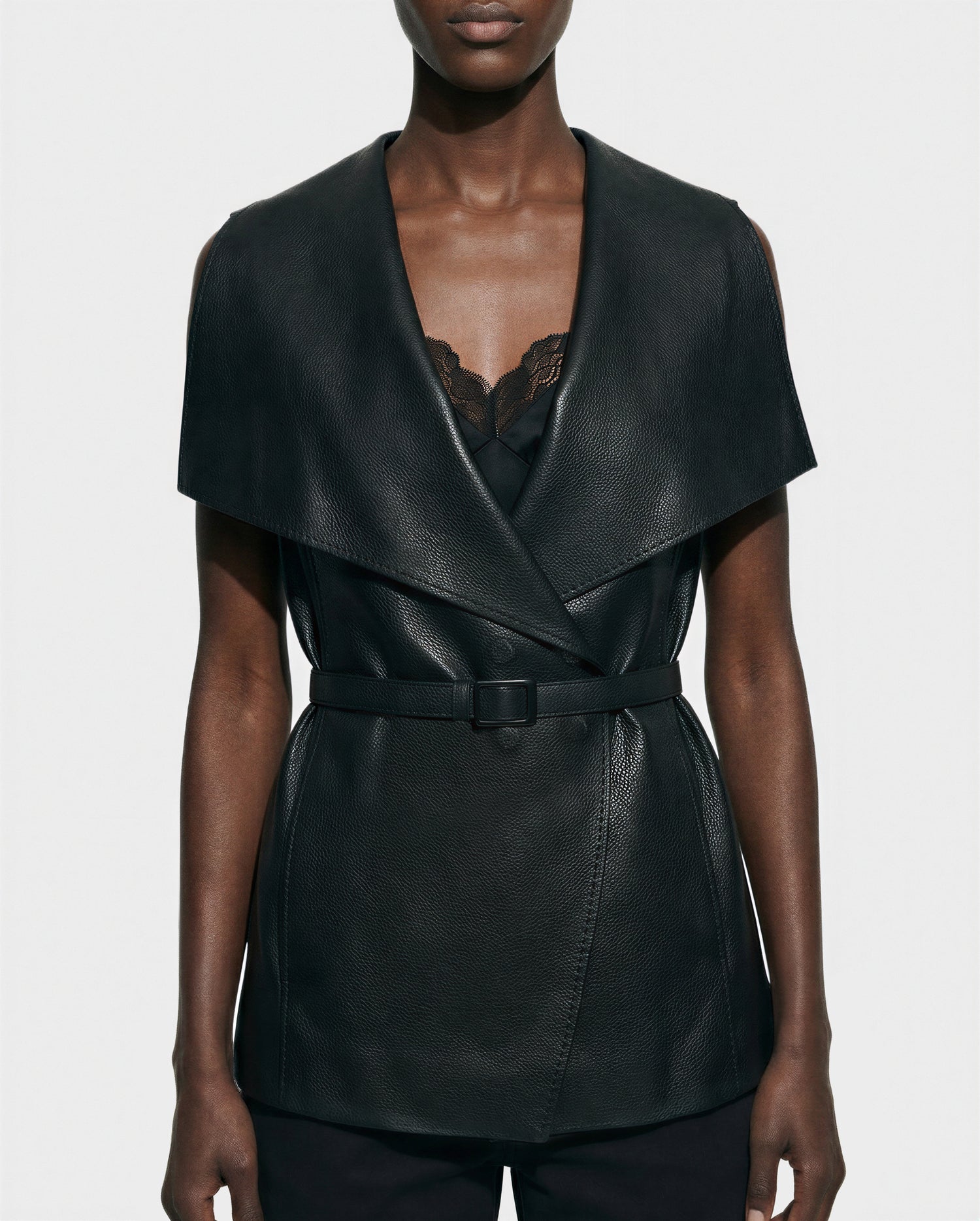 A person wears the Rudsak ELEANOR - 8125584 Black, a belted, sleeveless women’s leather vest with a wide shawl collar, layered over a lace-trimmed black top against a plain light background.