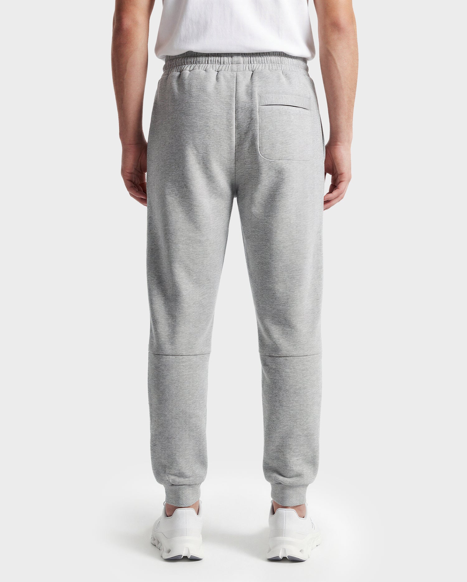 A person is seen from behind wearing Rudsak's JOSS - 9524009 Heather Grey M unisex jogger sweatpants with an elastic waistband and a single back pocket, styled with a white t-shirt and white sneakers.