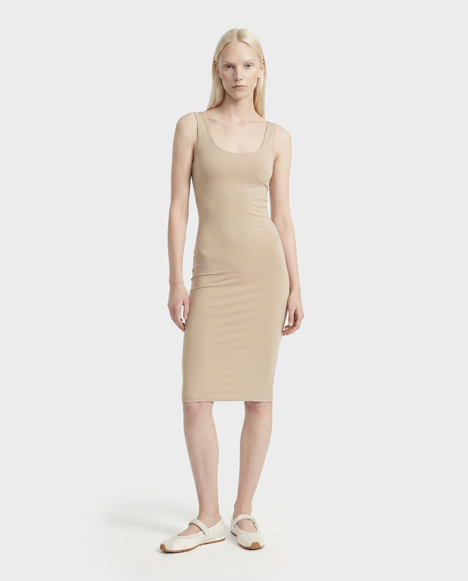 A woman with long blond hair wears the Rudsak DENISE - L523027 Cream fitted sleeveless midi dress and white flats, standing against a plain white background.