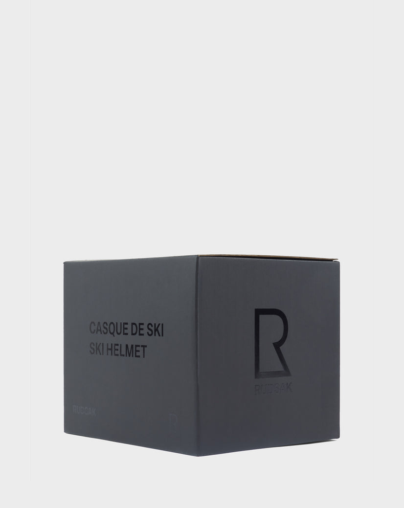 A dark gray Rudsak box with "CASQUE DE SKI SKI HELMET" text and a large R logo on the side, set against a plain light background—featuring the RACE - 9421514 POPPY RED from the exclusive Ski Capsule Collection.