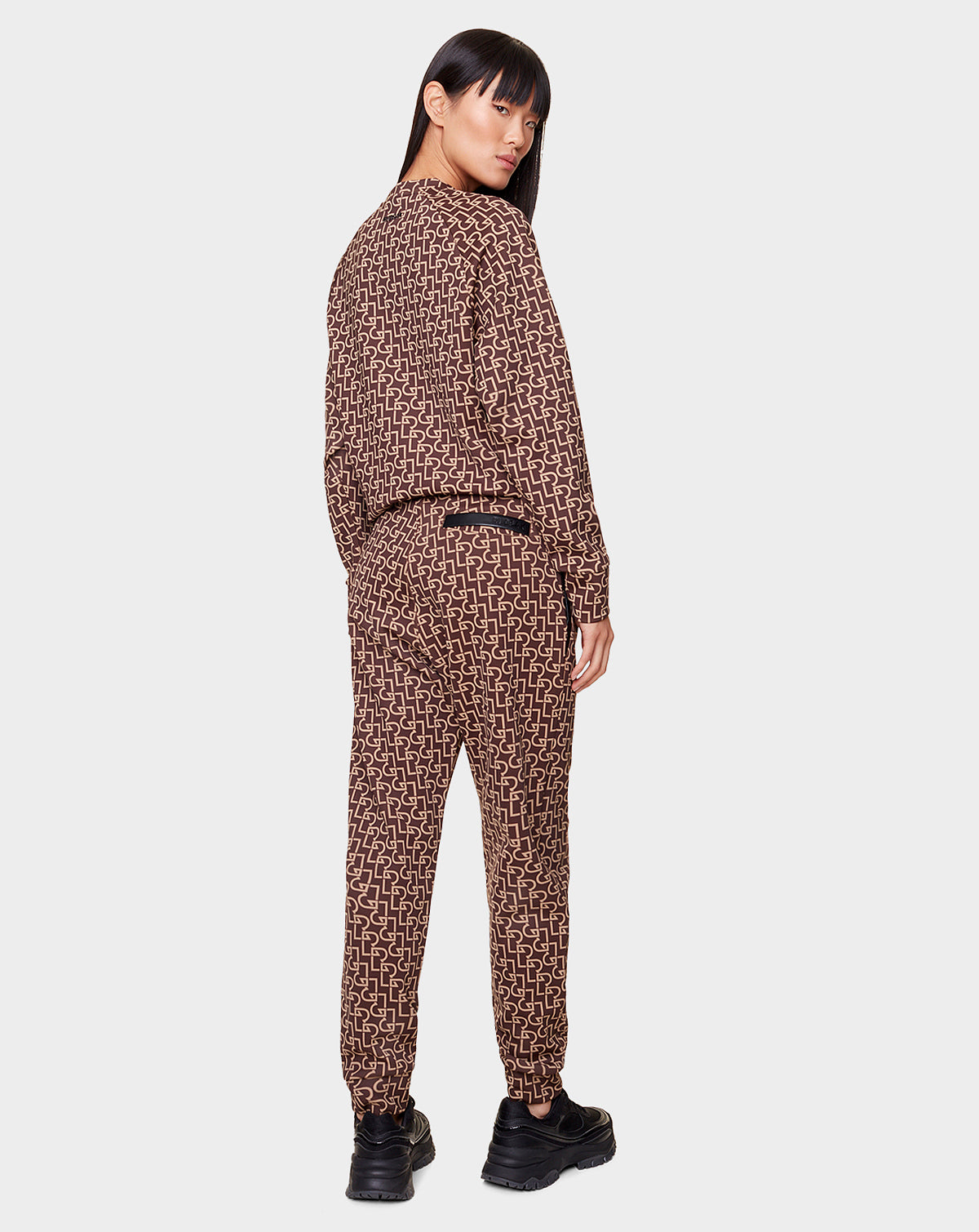 A person faces away, turning their head to the side, wearing Rudsak OLAV - 9522503 RUDSAK PATTERN WOMEN joggers and matching top with black chunky shoes on a plain light gray background.