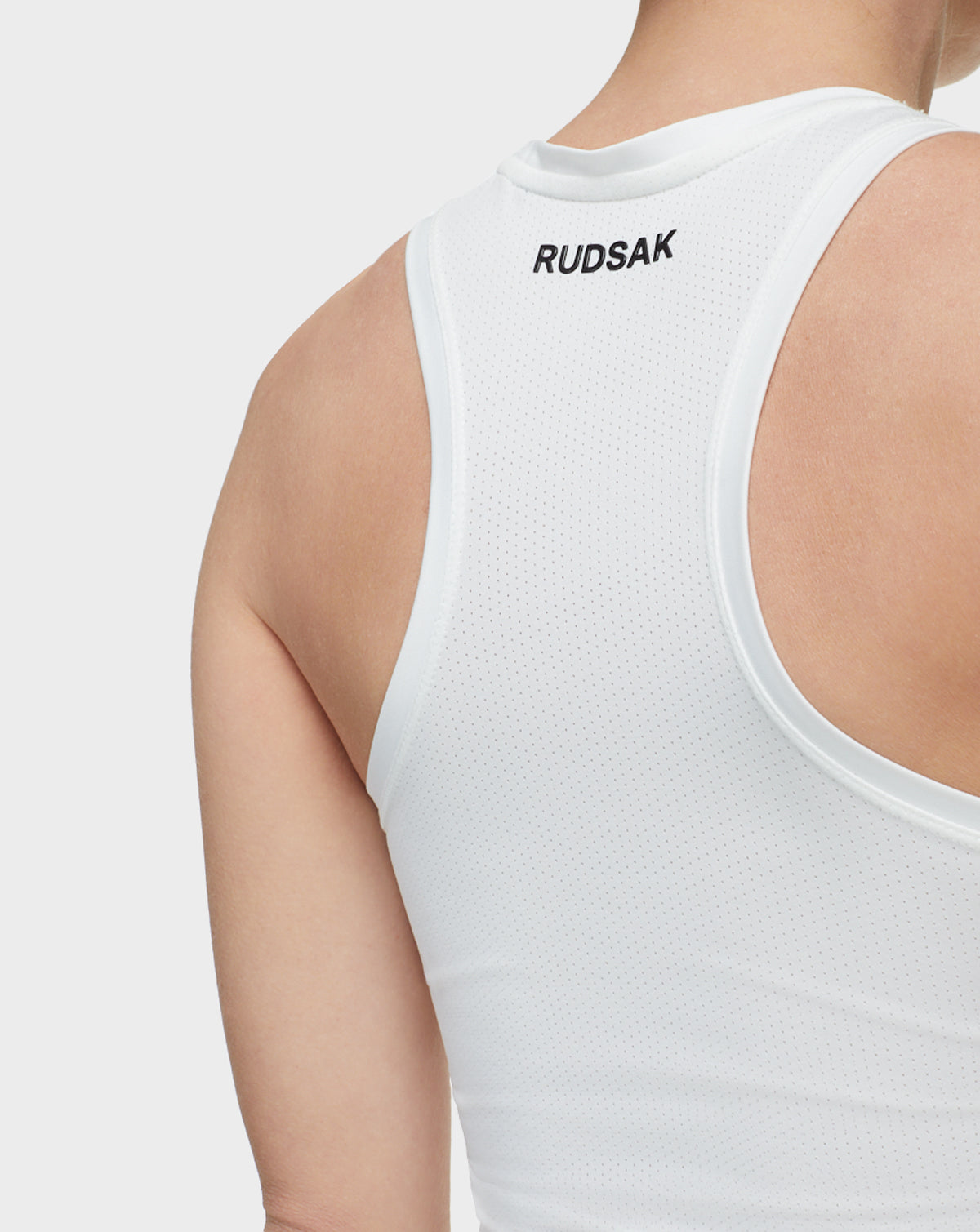 Close-up of a person wearing the Rudsak SABIE - 8522020 WHITE sleeveless athletic top, featuring the Rudsak logo in black on the upper back, with focus on the shoulder and upper back.